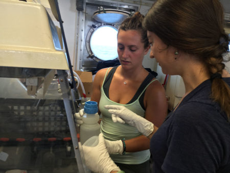 Jessica Kendall-Bar (left) and Hannah Bourne get hands-on experience working with water samples in the field. They are shown here filtering out the particles from water samples collected by the CTD. (Photo: Sarah Yang)